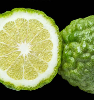 Fresh bergamot fruit with vibrant green skin and a sliced half showing the juicy yellow interior.